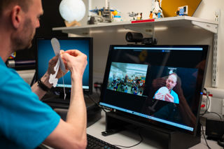An Education Presenter holding a paper earth with paper satellites attached, presenting to a school group on a Video Conference.