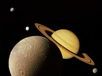 A moon is in the foreground, Saturn is just behind. A few celestial bodies are scattered further away, on a black background.