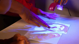 A child finger painting while under a UV light.